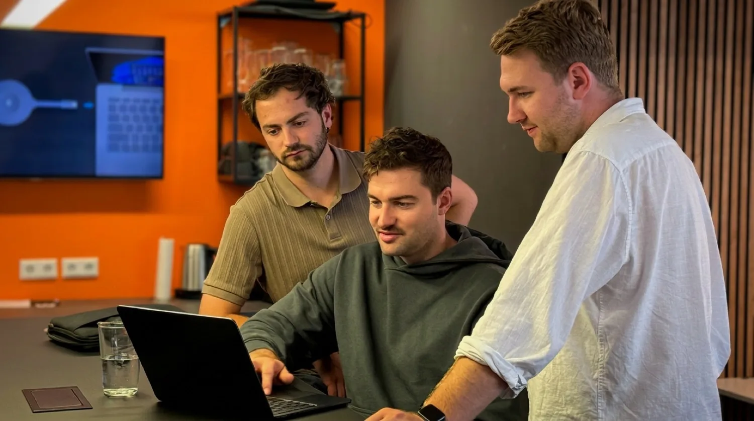 Sascha und sein Team schauen gemeinsam auf einen Laptop im Büro